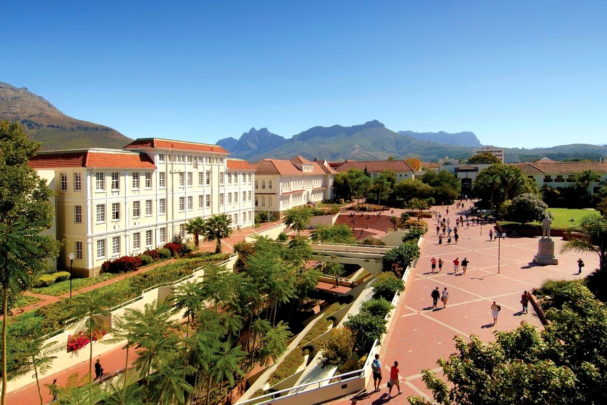 A landscaped garden and broad walkway beside a public building with mountains in the distance.