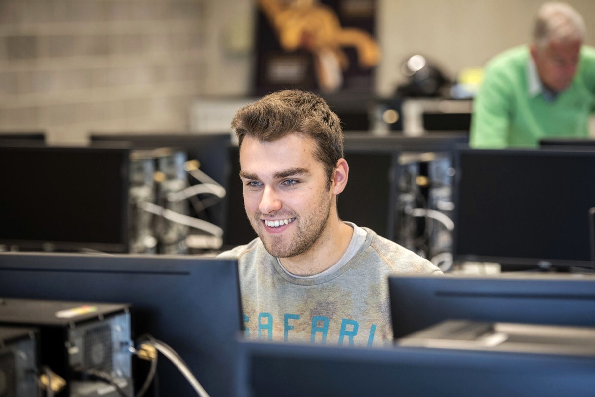 A person working at a computer in a bright shared editorial workspace.