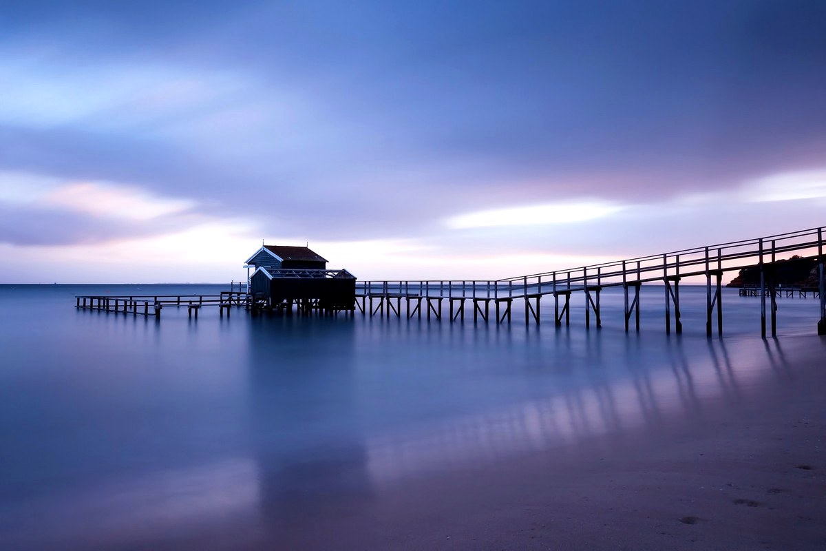 A long wooden pier extending over calm water under a blue and violet evening sky.