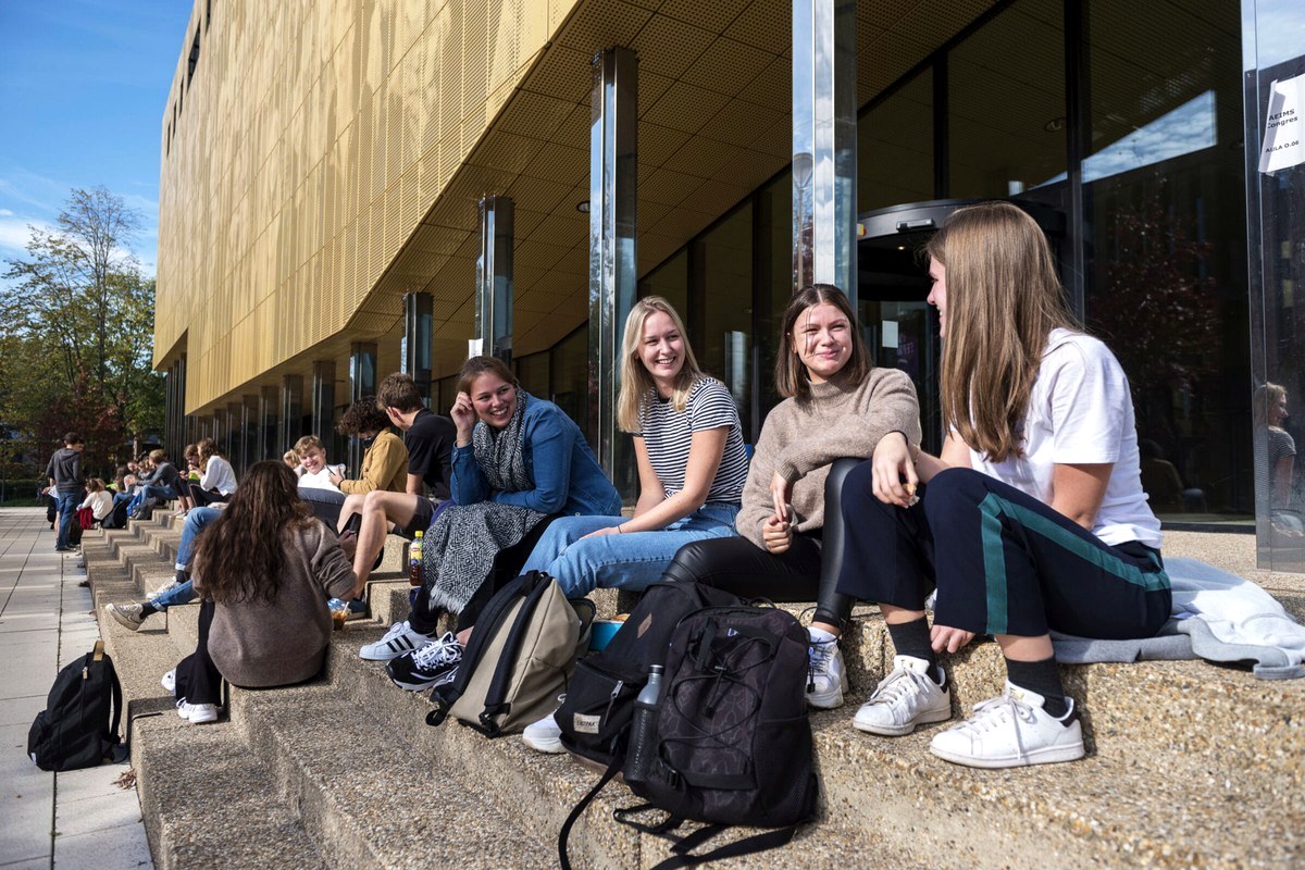 A group of people sitting together outside a modern public building.
